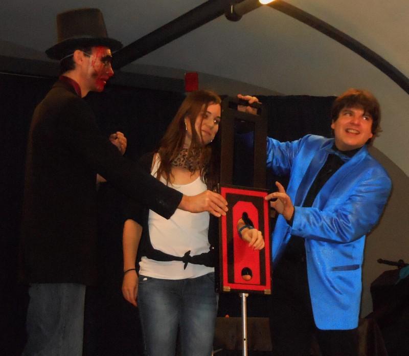 Magicien Olivier OK MAGICS présentant la Guillotine au Bras avec une spectatrice durant le Halloween Tour 2013